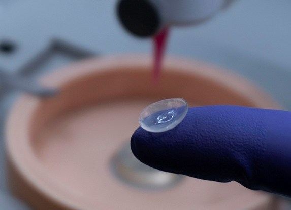 A transparent bioprinted corneal disc balanced on a gloved fingertip